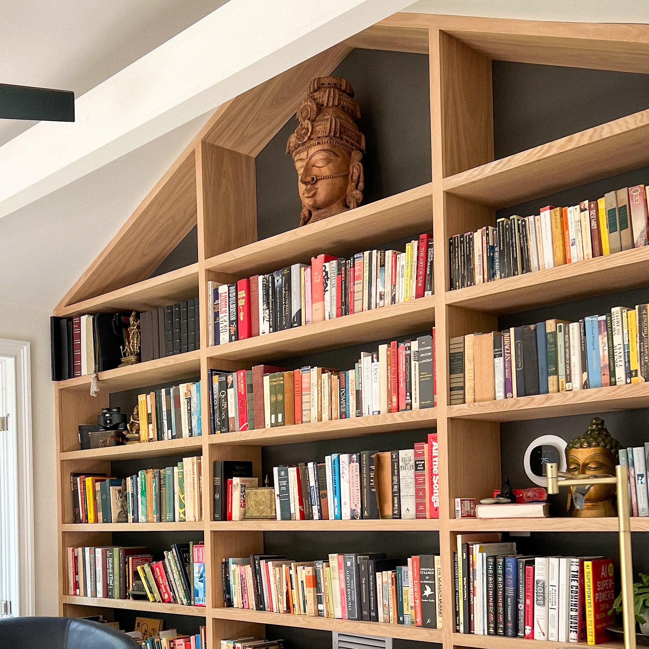 Wooden bookshelf filled with books and decorative items in a room with a sloped ceiling.